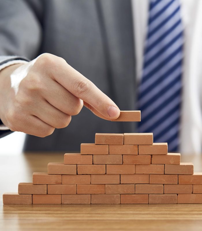 businessman-suit-putting-last-piece-pyramid-using-wooden-blocks-min
